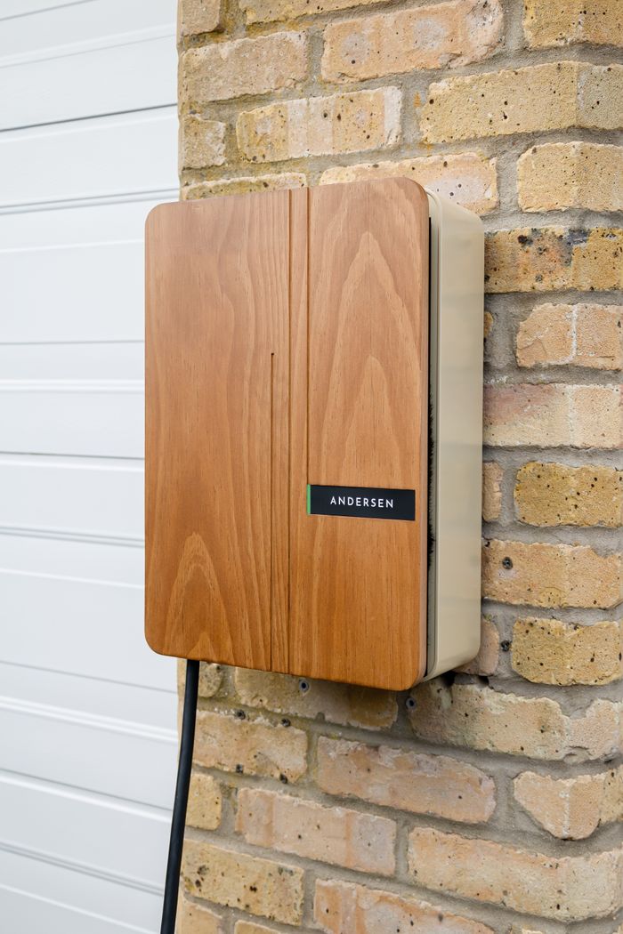 Wood-paneled Andersen electric vehicle charger mounted on a home's brick exterior.